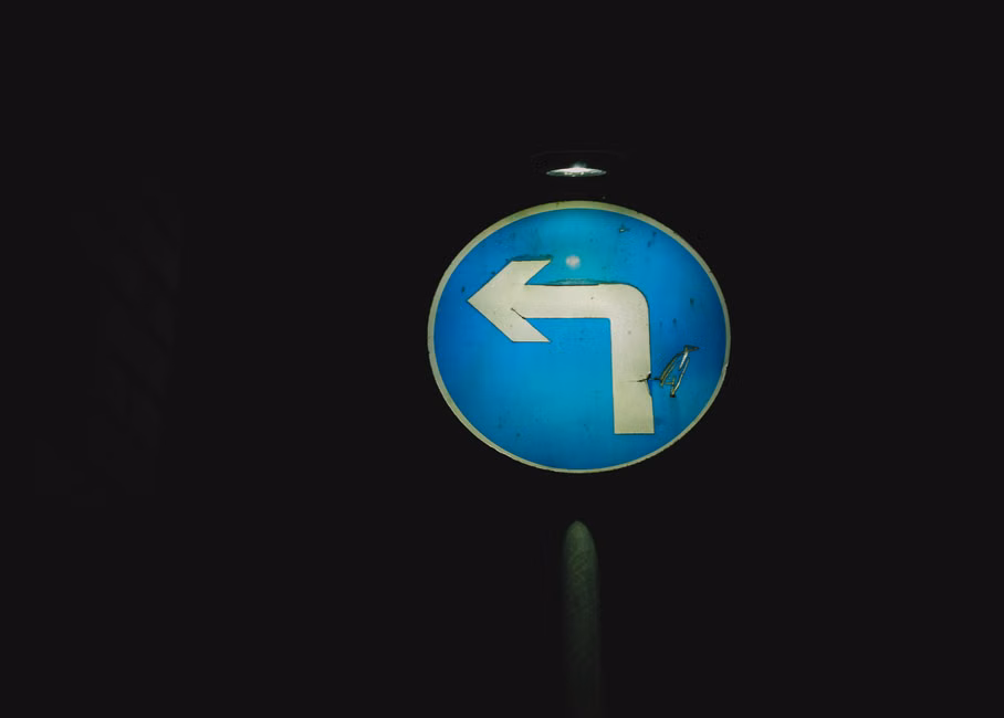 Round old left turn sign on blue background with light at dark night